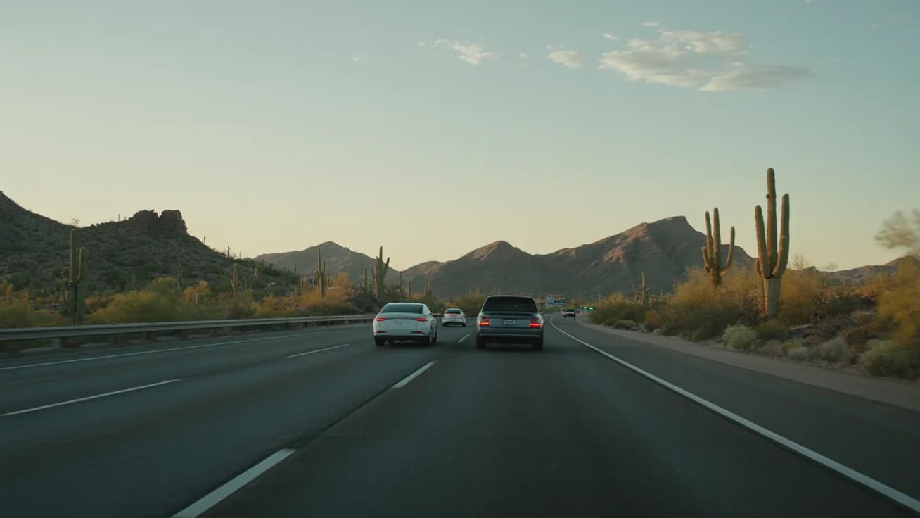 Vehicles on an Arizona highway at sunset with desert mountains in the background